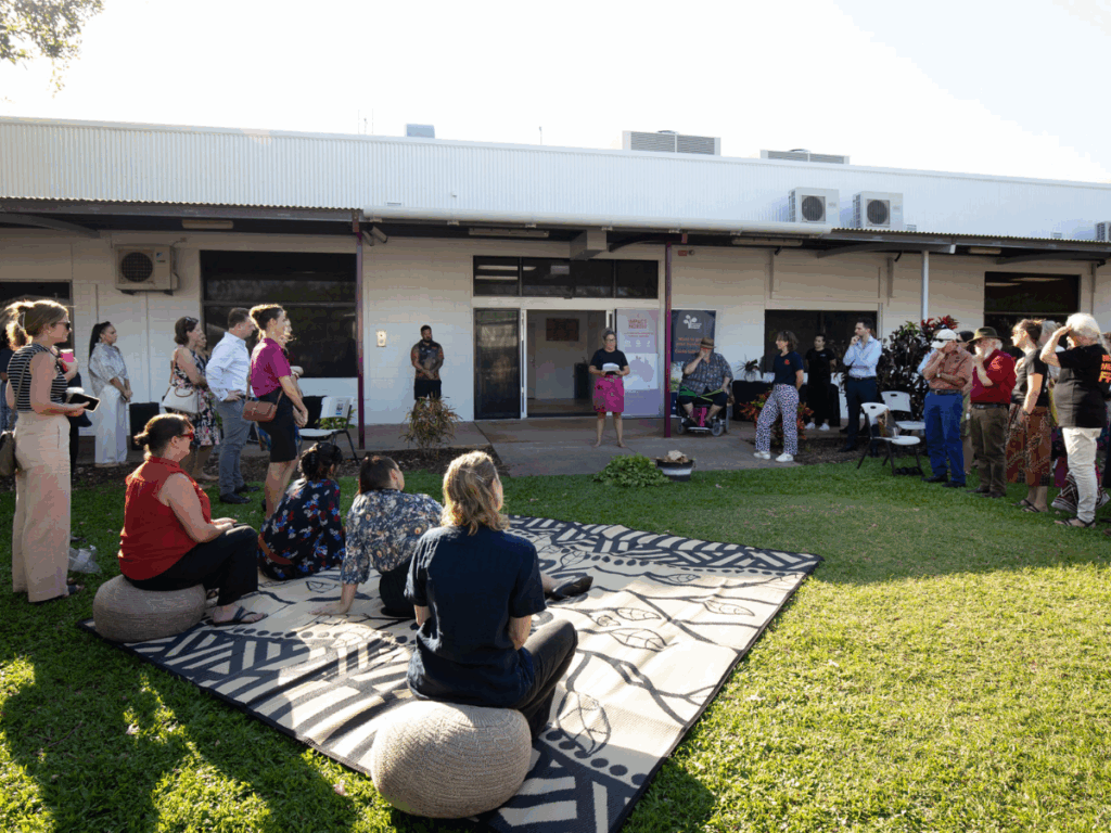A group of people are gathered on the grass outside of a building.
