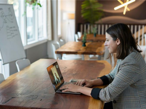 Women at desk with laptop in online session. There's a whiteboard in the background.