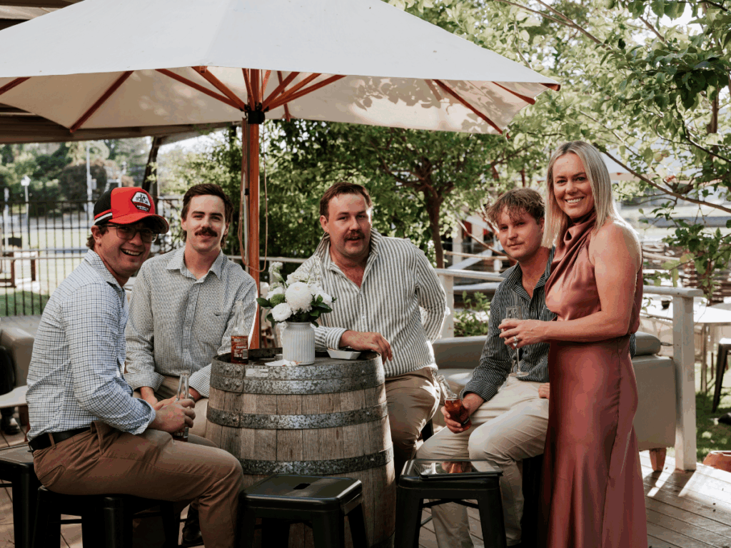 A group of people are dressed formally and seated around a beer barrel-table at an event. 