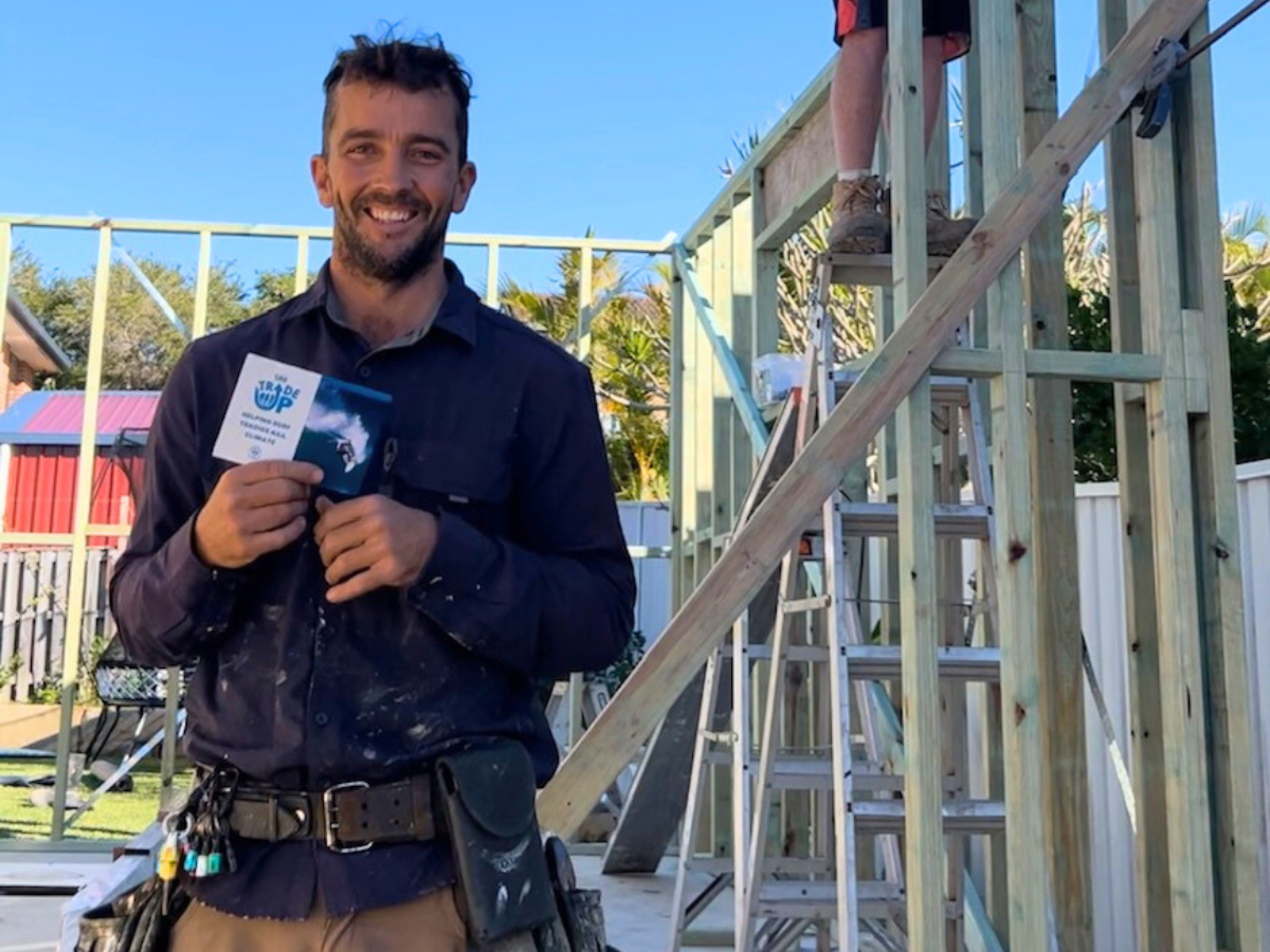 A man stands holding up a leaflet next to scaffolding. 