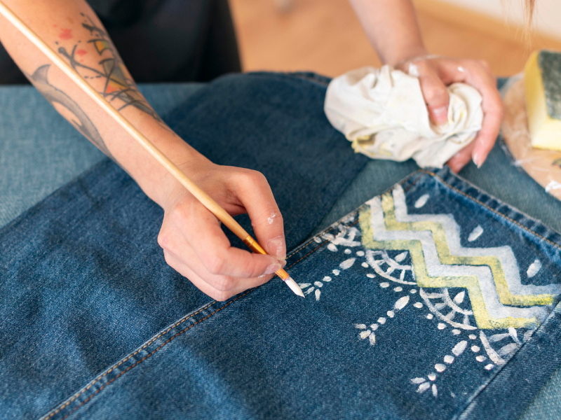 Close up of hand holding paintbrush, painting a pattern onto jeans.