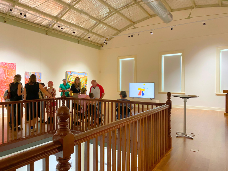 Image of a light and spacious gallery with a group of people standing behind the stair banister.