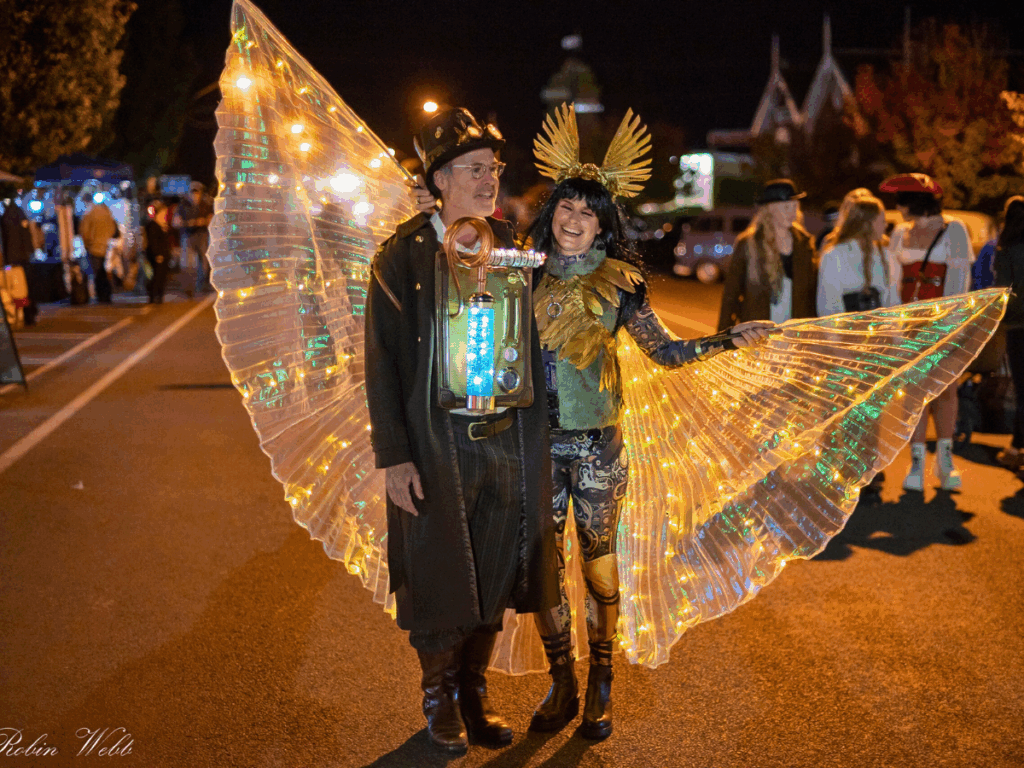 Two people with a crowd behind them. One of the people is wearing decorated wings as part of a costume.