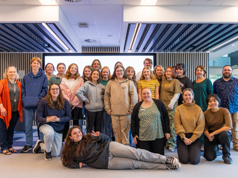 A large group of people stand for a photo with one woman laying sideways in front of the group.