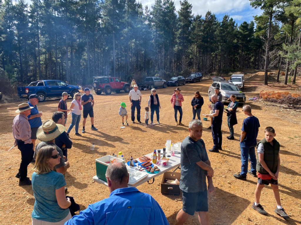 Group of people gathered for an event in a clearing surrounded by trees.