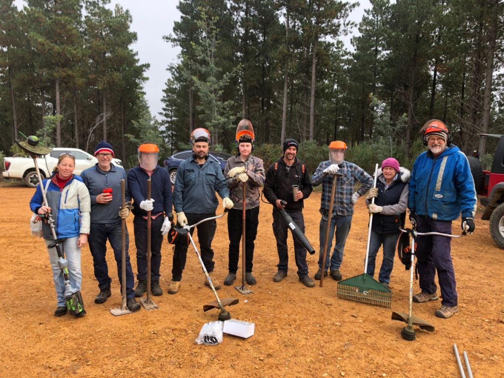 A group of people stand together with various tools, smiling for the camera.