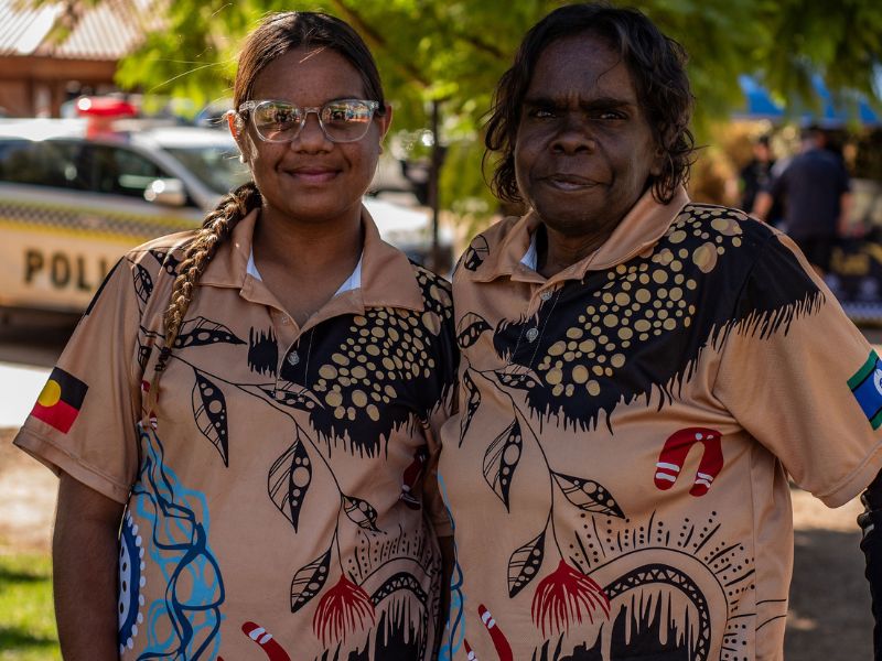 Two women stand side-by-side smiling at the camera, wearing colourful t-shirts.