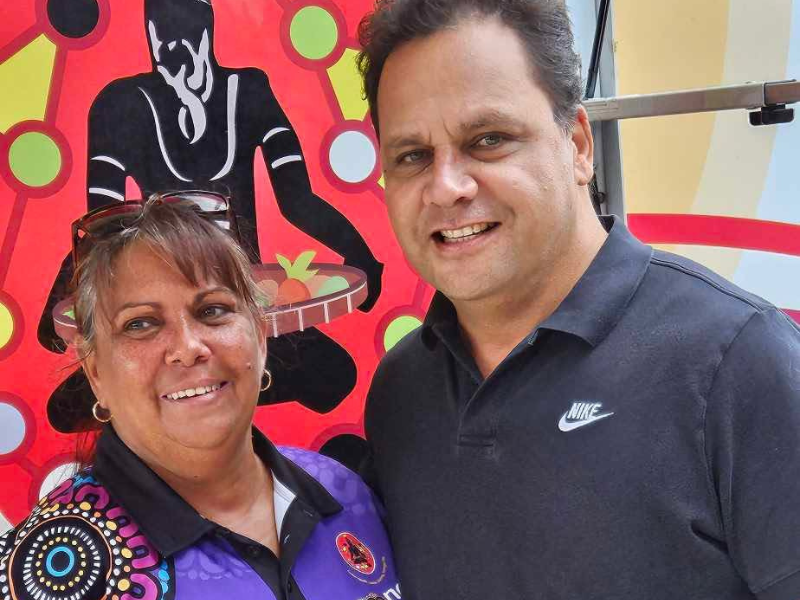 Two people smile for the camera with a colourful piece of art behind them.