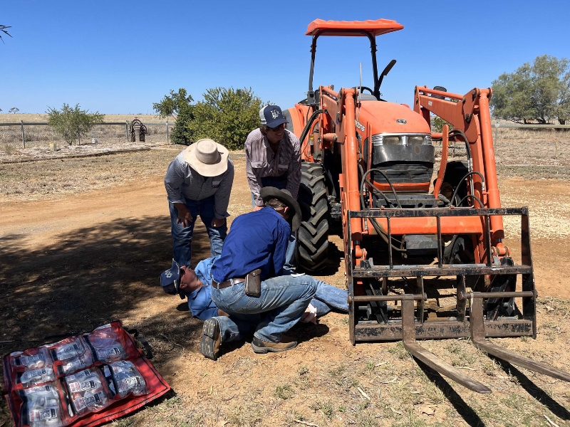 Group of people gathered in a mock first aid scenario outdoors near a tractor. 