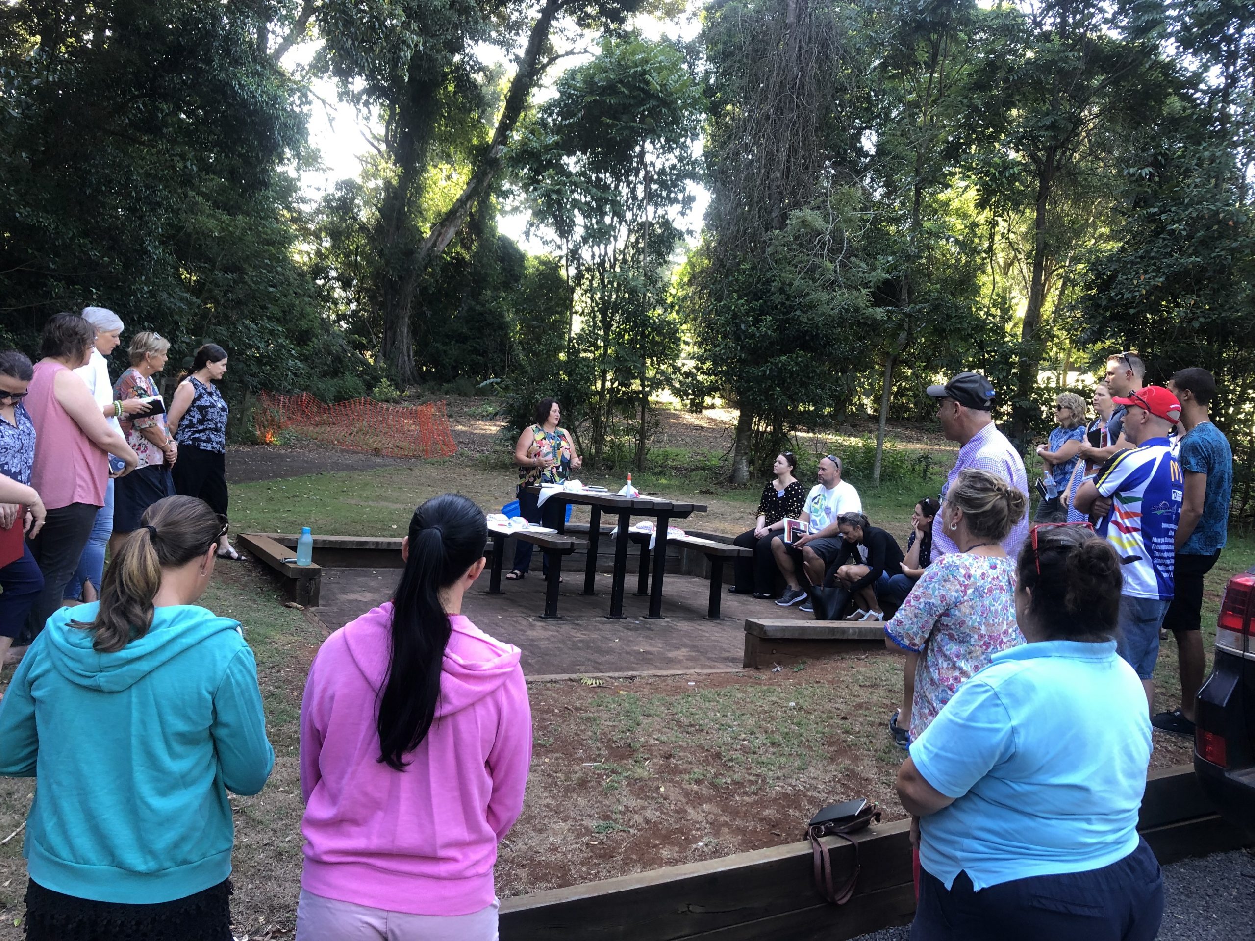 A group of people gather around a central table, in a park, working together and chatting