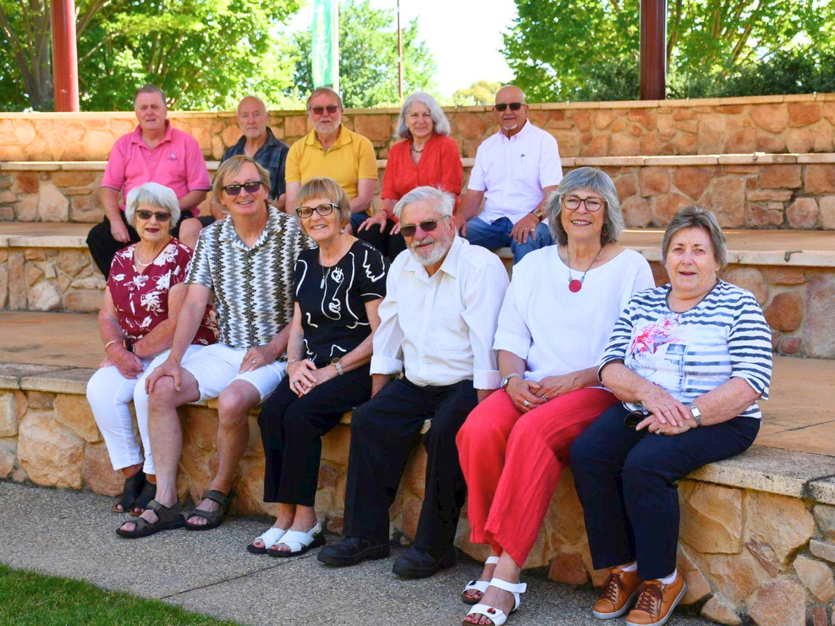 Group of people sitting on stone steps outdoors with greenery behind them.