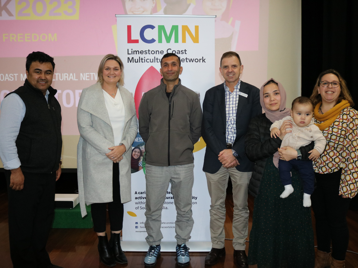 Group of people stand on-stage in front of a presentation screen at an event.