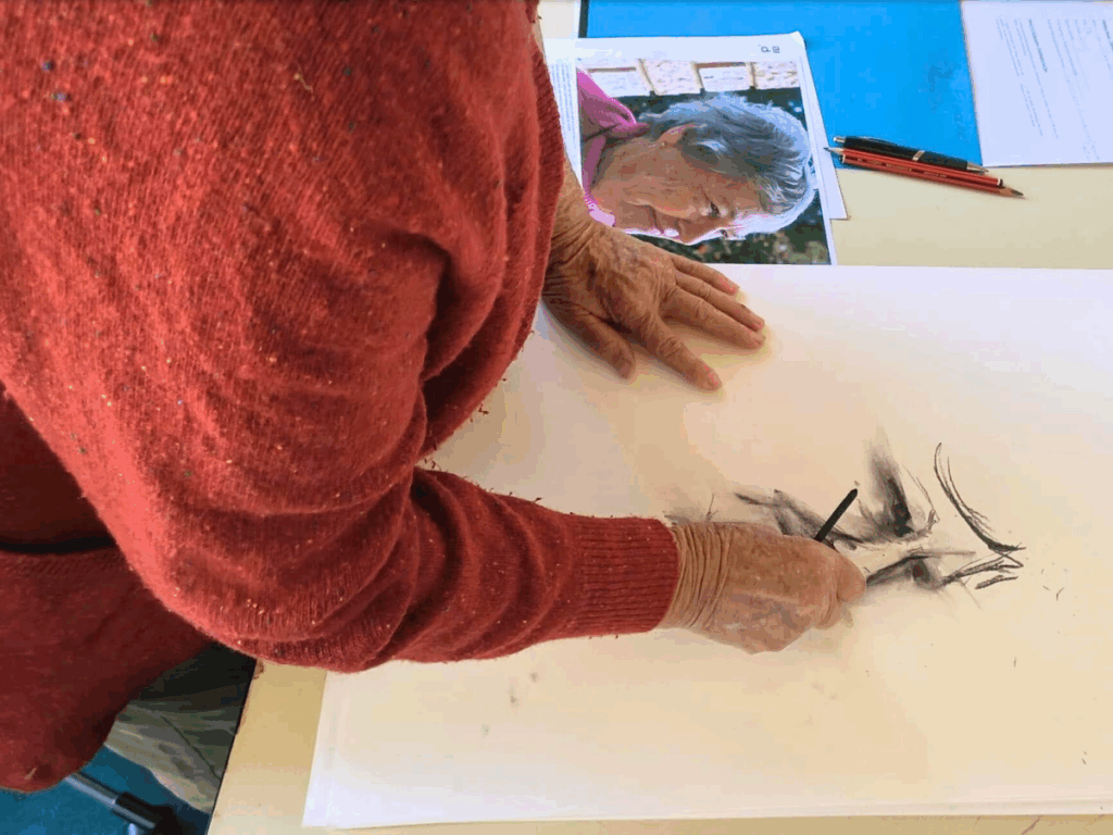 Close up of woman in a red cardigan drawing a portrait of herself. 