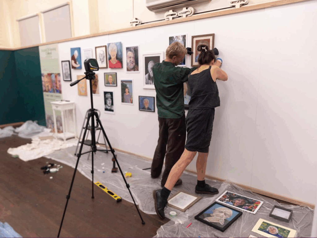 Two people are putting a painting on a pop up exhibition wall. 