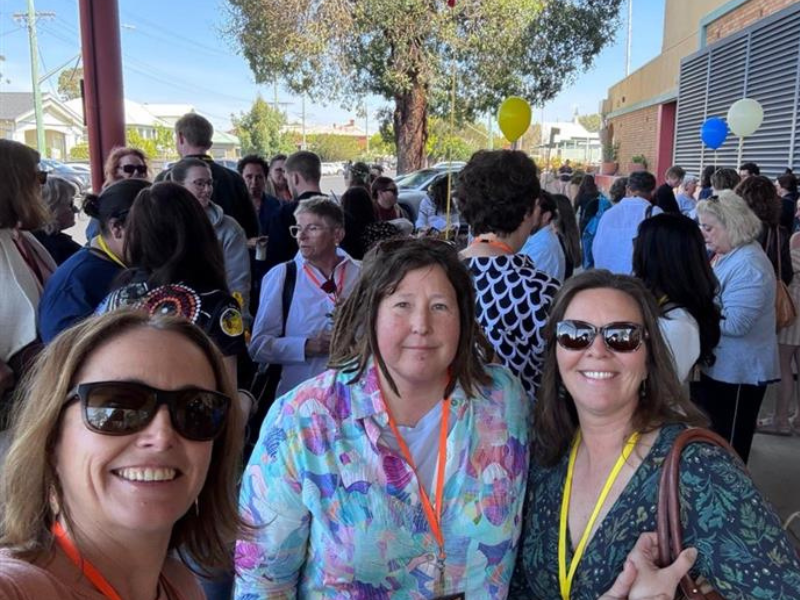 Three women in the foreground looking at the camera with a crowd of people behind them.