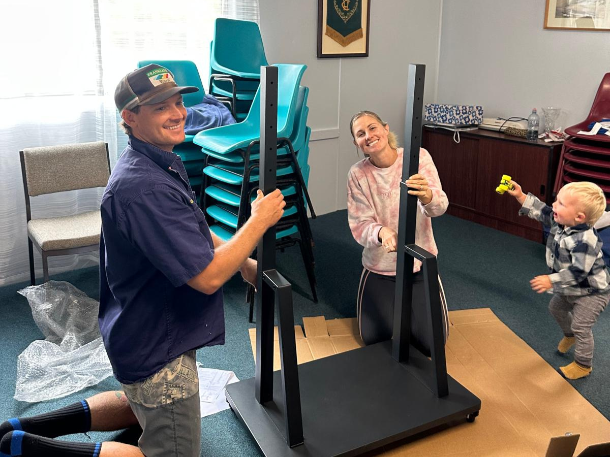 A man, woman and baby are shown to be assembling a piece of black furniture, all smiling. 