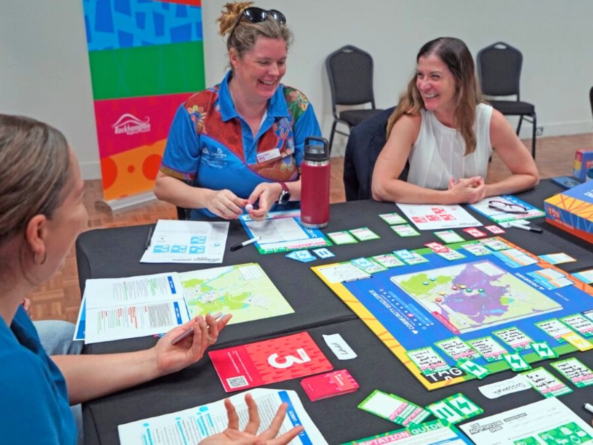 Three women are gathered around a table playing a game with a colourful board. 