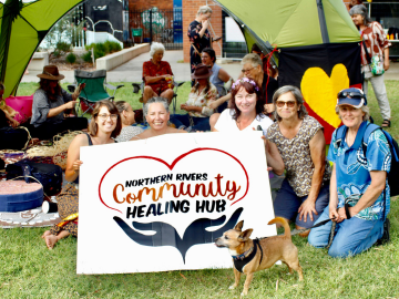People sitting on the ground with a sign in front of them.
