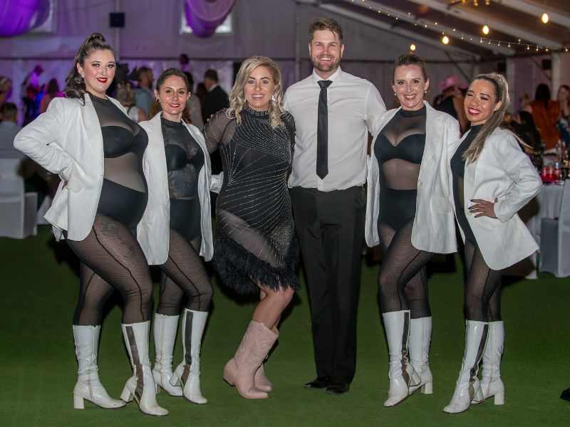 A group of women and one man stand posing for their picture, dressed in black and white sparkly outfits. 