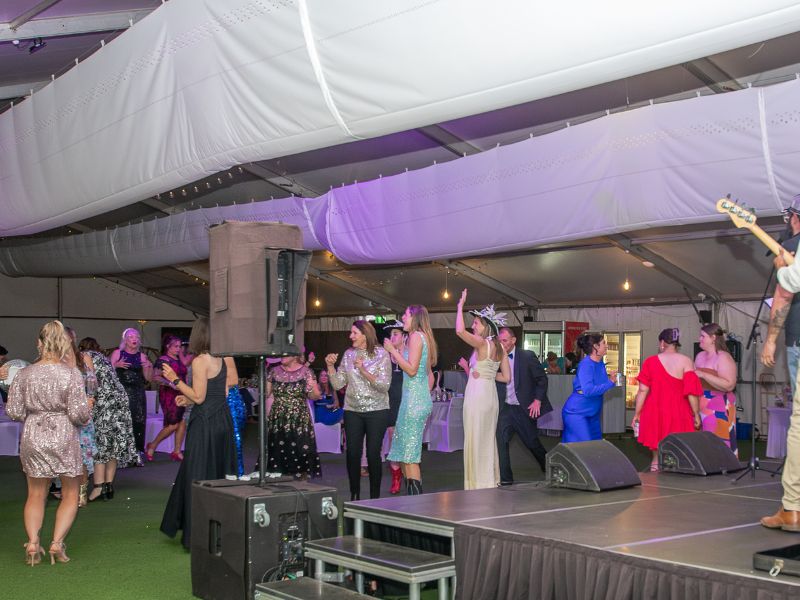 A band is playing on stage and a large group of people are dancing on the dancefloor. 