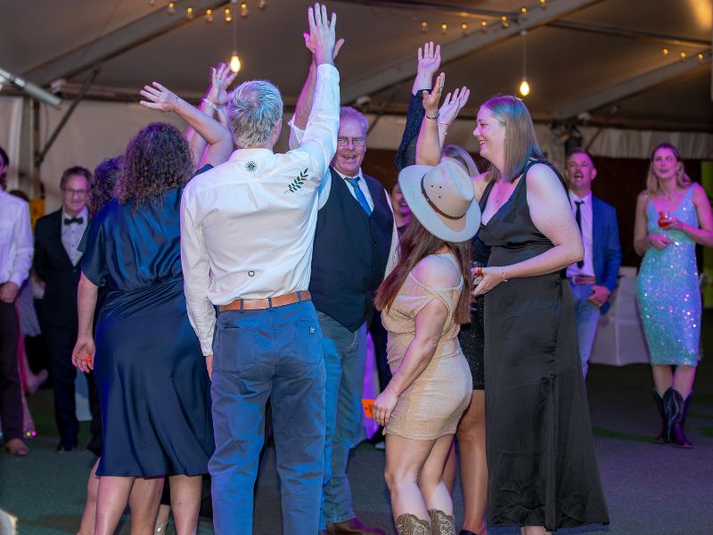 A group of people are huddled close together on the dance floor with their hands up in the air. 