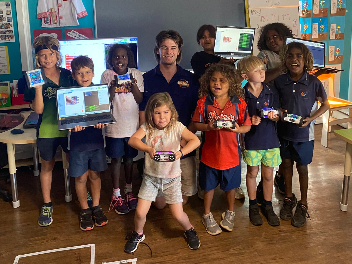 Man crouched with group of primary aged children in classroom. 