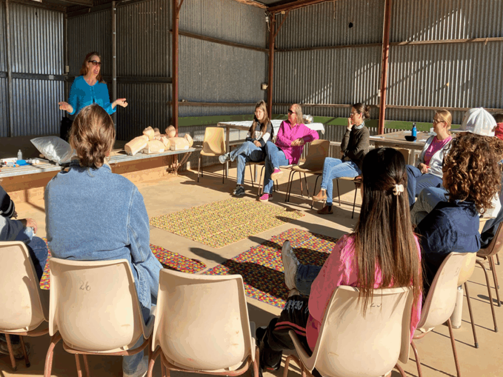 A woman is talking in front of group of people seated on plastic chairs in a circle. 