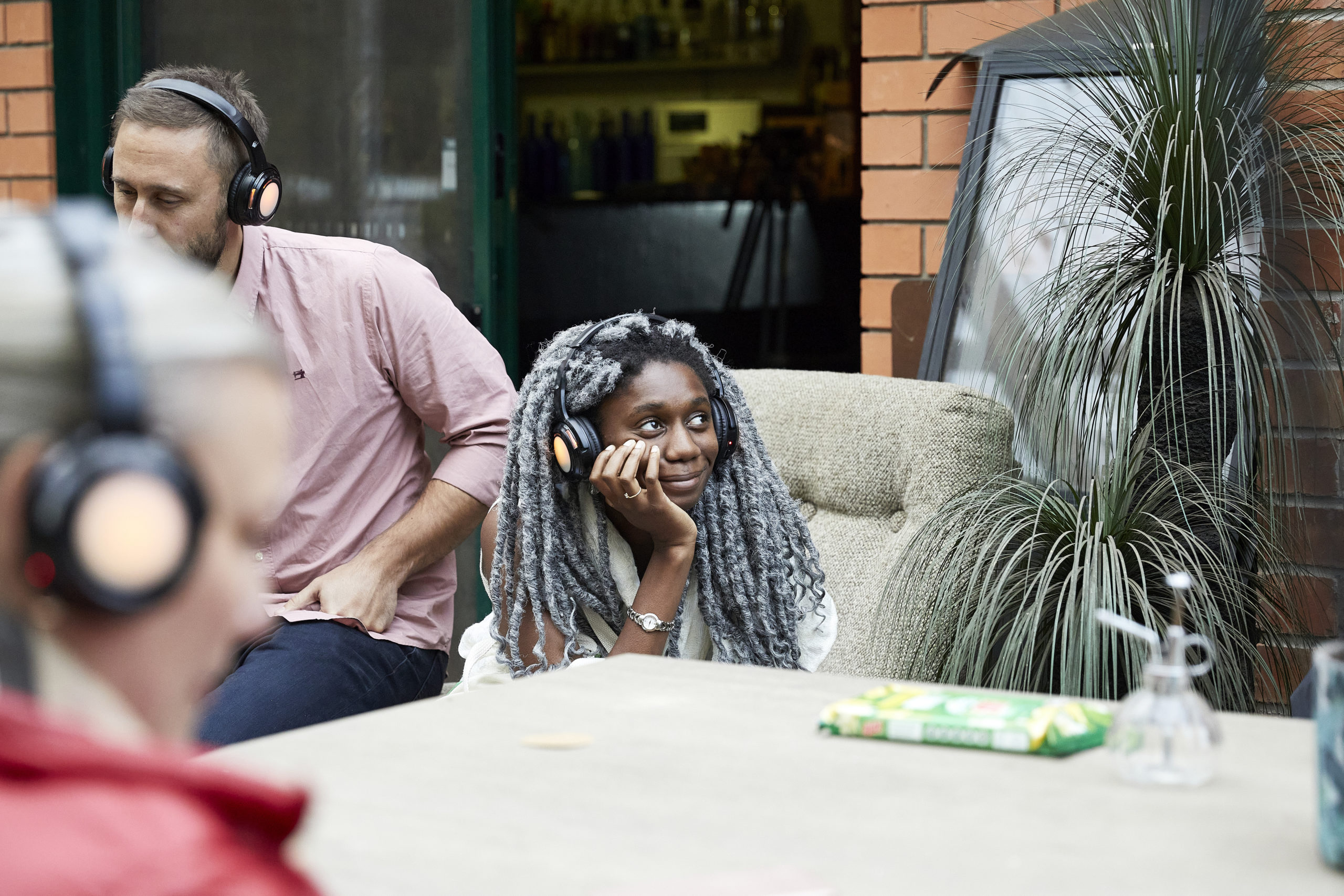Young people sit on a couch, listening to podcasts through headphones