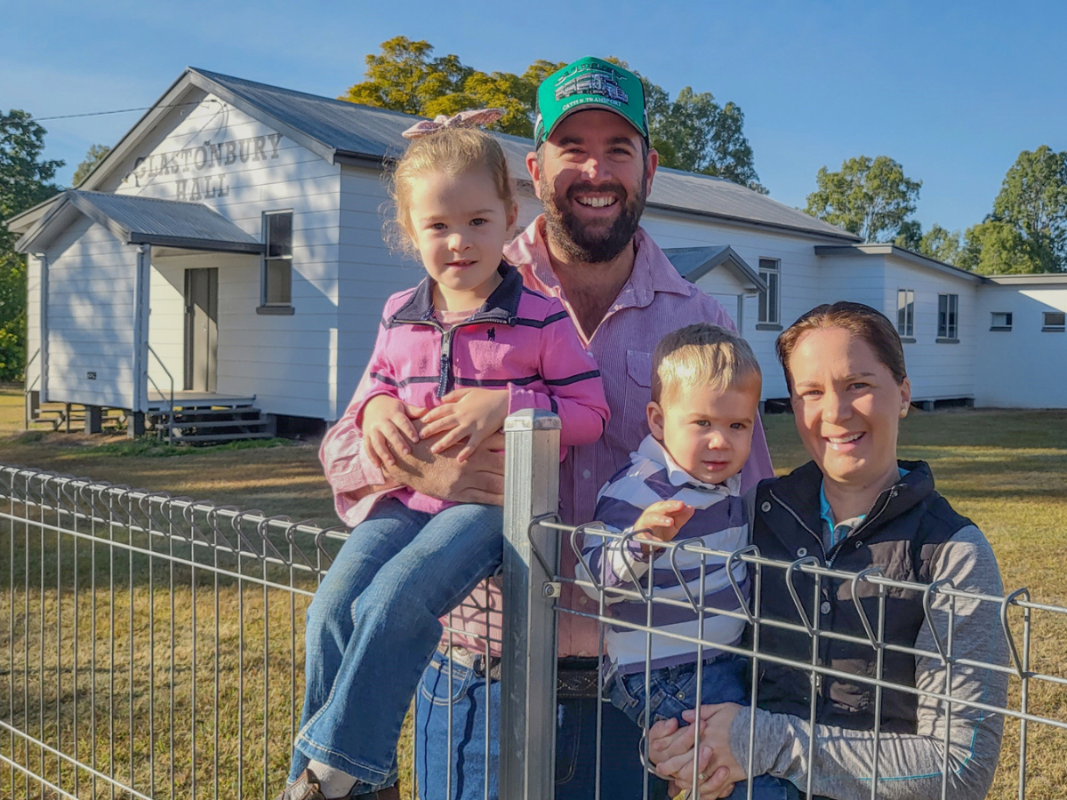 Family of four leaning on wire fence in front of the Glastonbury Hall.