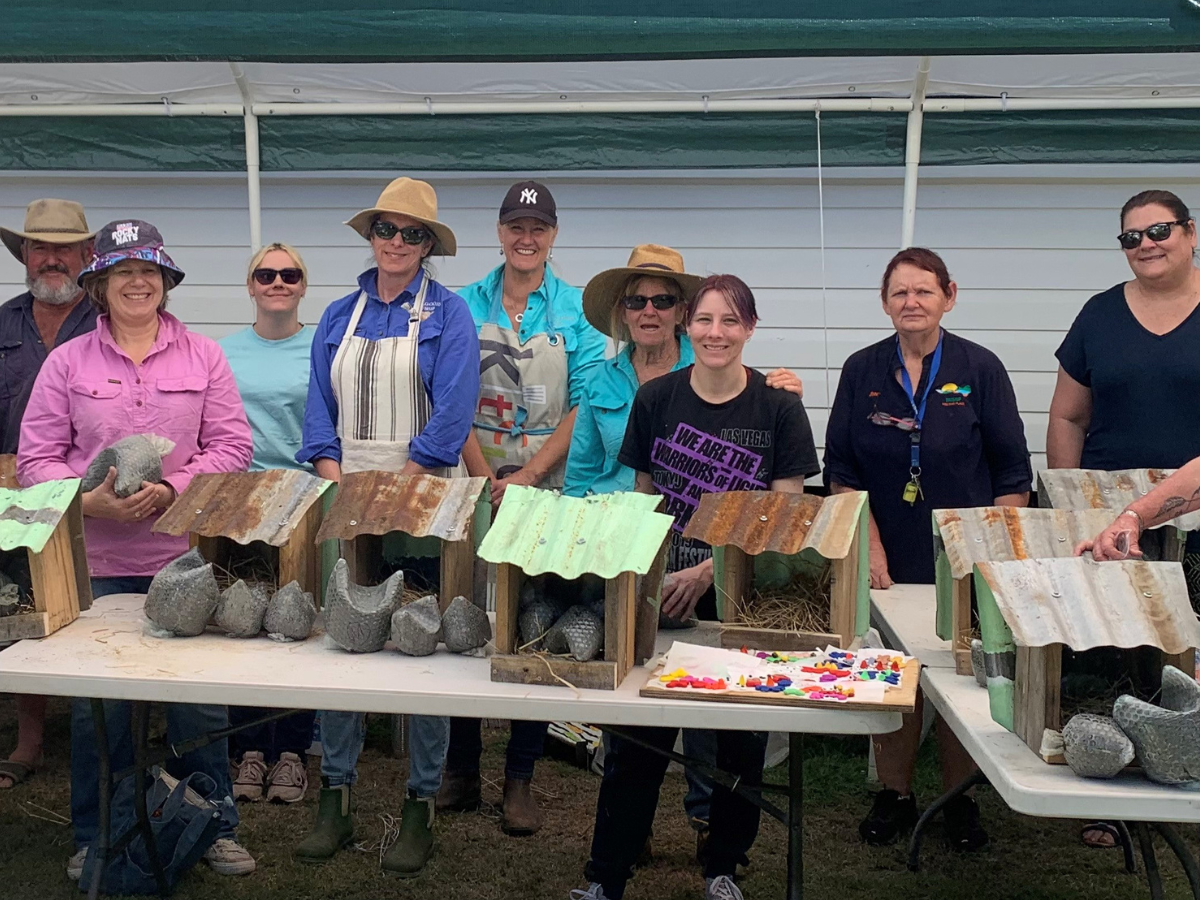 Group of people standing under a marquee behind a table full of handcrafted wares.
