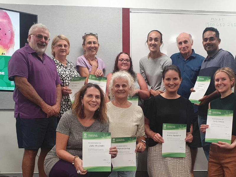 Group of people pose with certificates in a classroom.