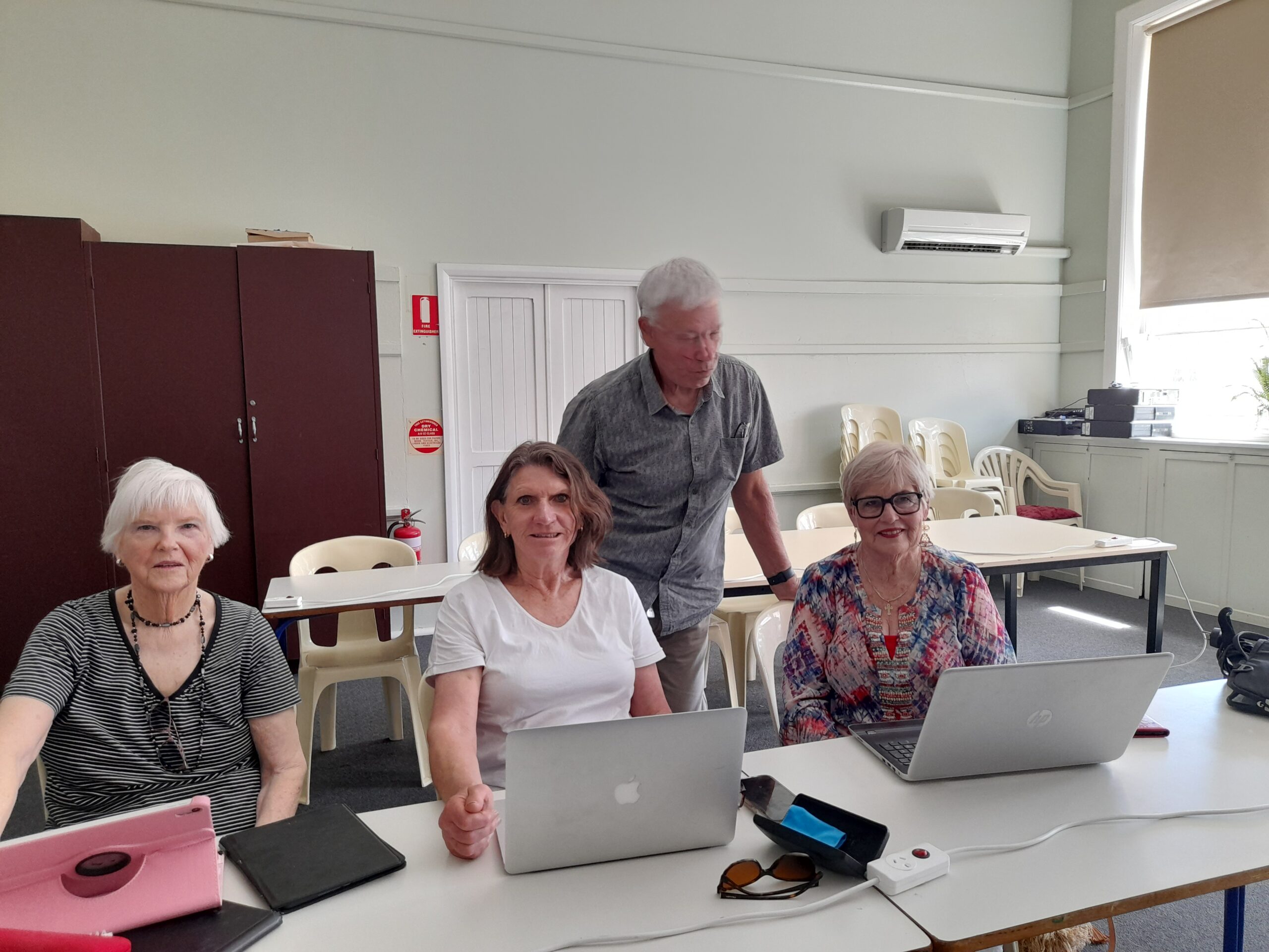 Four people sitting in a classroom with computers.