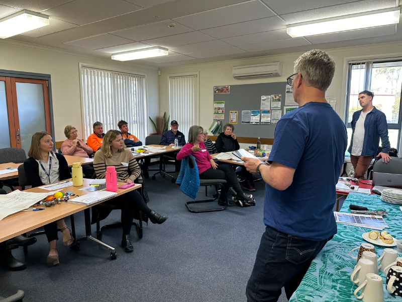 Person stands in front of seated onlookers in classroom.