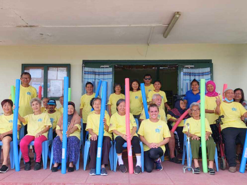 Group of people standing in yellow t-shirts with pool noodles. 