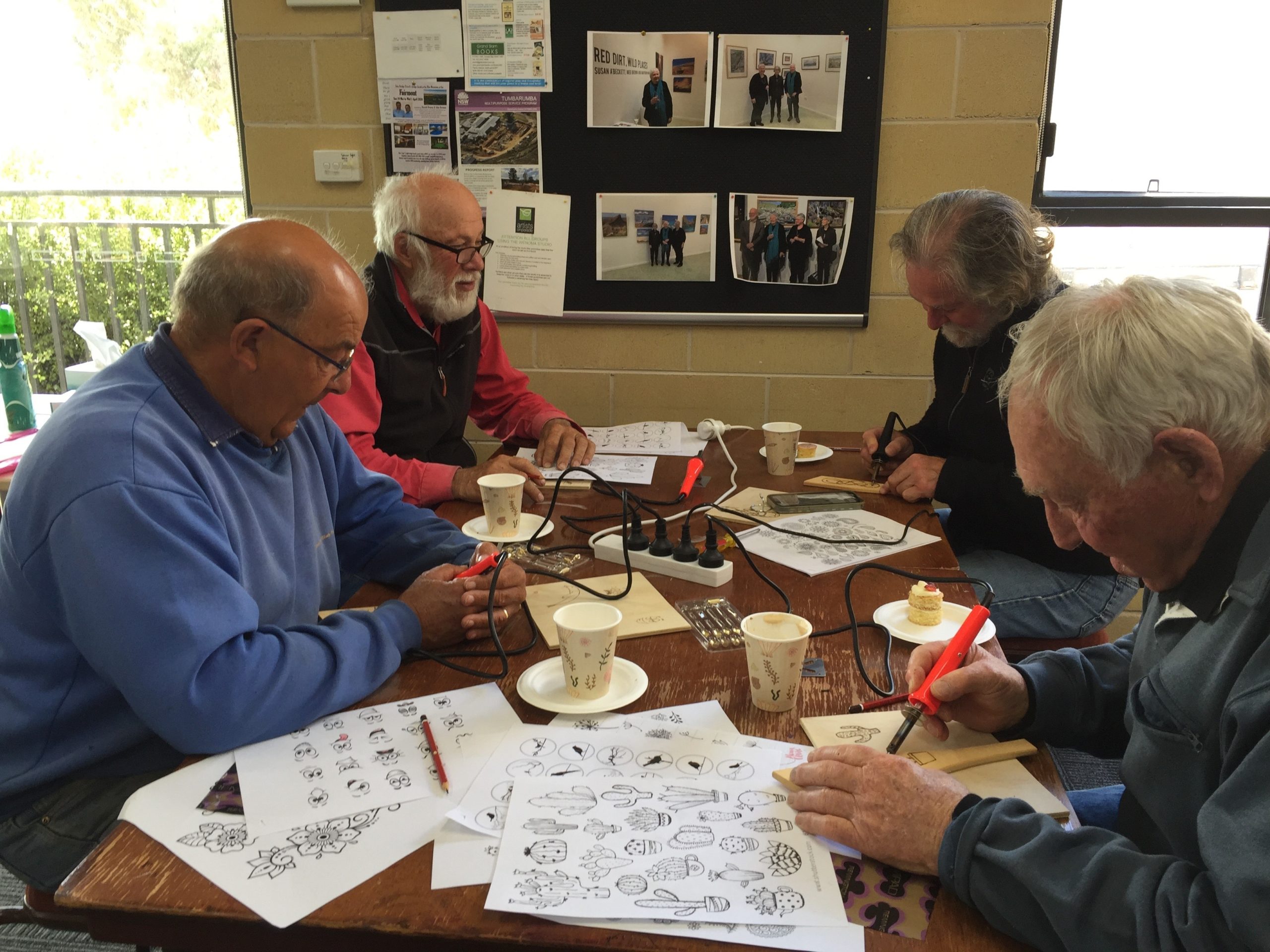 Four men sit at a table practising woodburning crafts