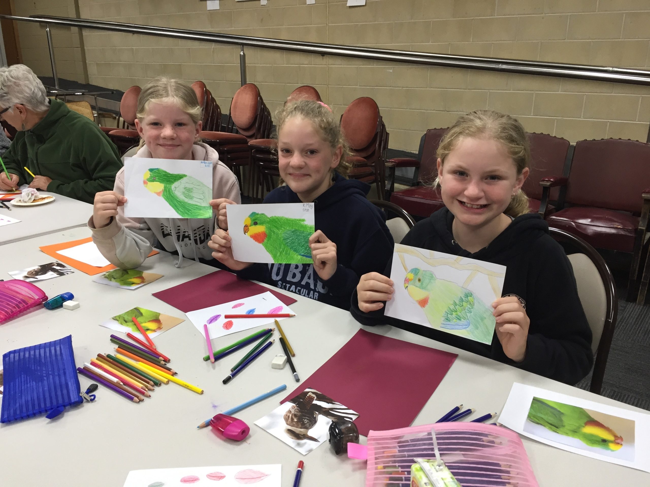 Three young girls show off their drawings of parrots
