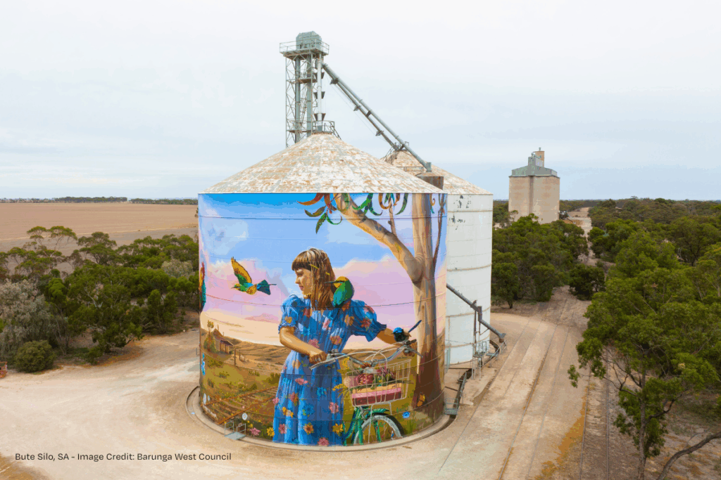 Grain silo with mural of a girl and her bike with a rural landscape in the background.