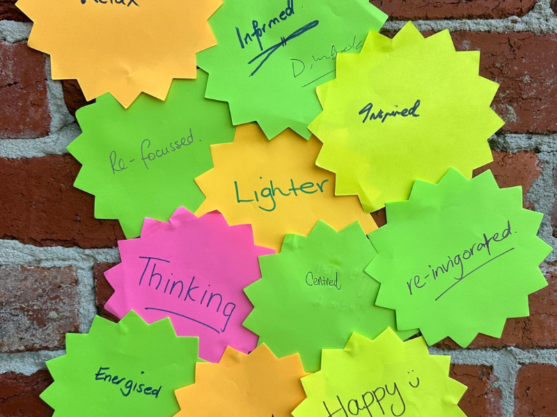 Close up of star shaped post-it notes with various one-word notes on them in yellow, orange, green and pink on a brick wall background. 