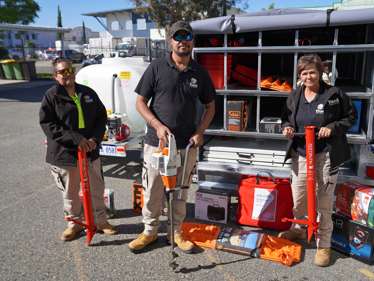 Three people standing in front of gardening tools.
