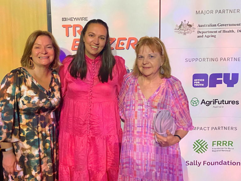 Three women standing together in front of a media board.