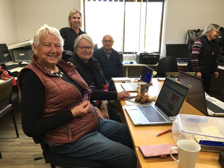 Older people sitting at a desk with a computer on it.