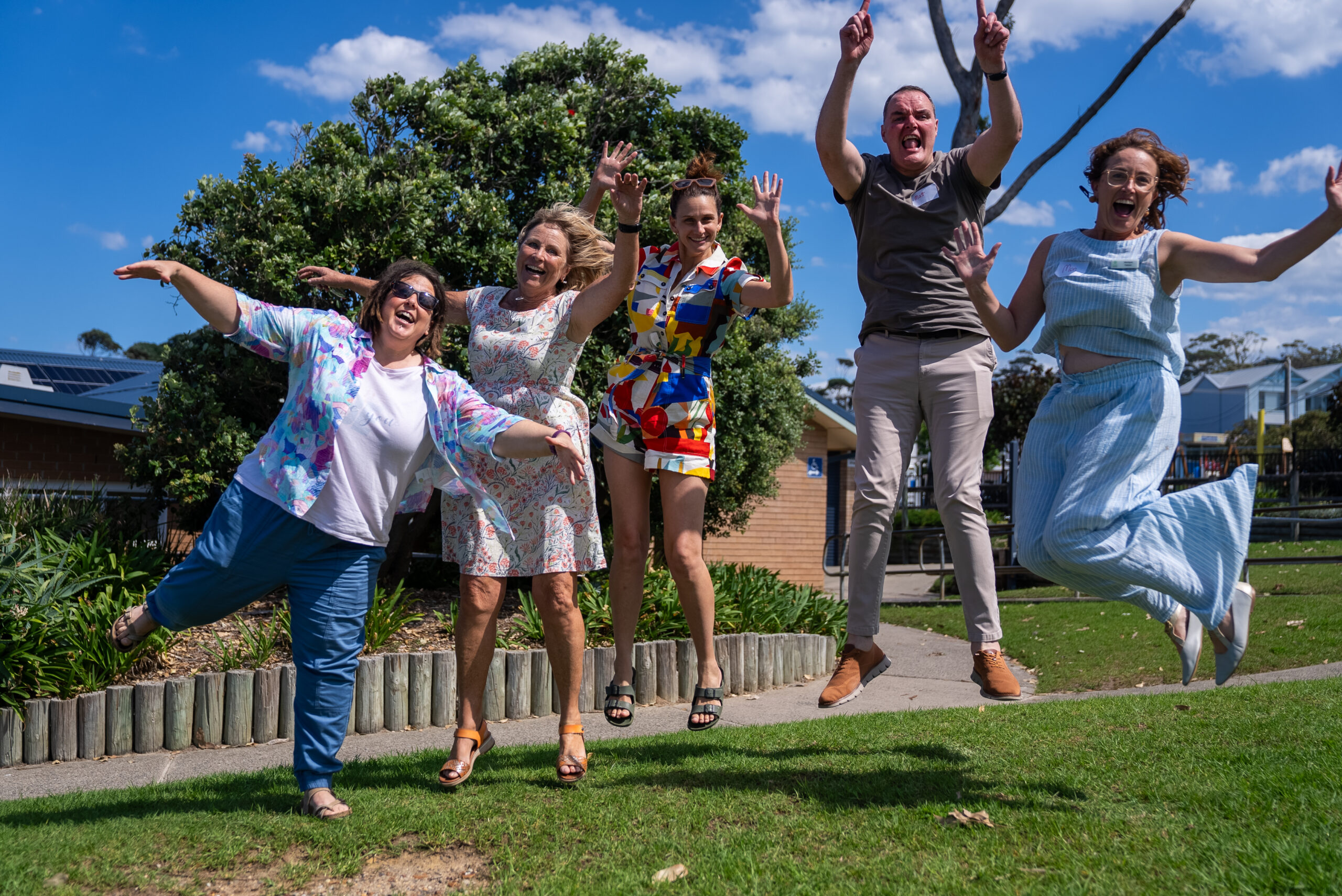 Five adults jumping joyfully outdoors on grass