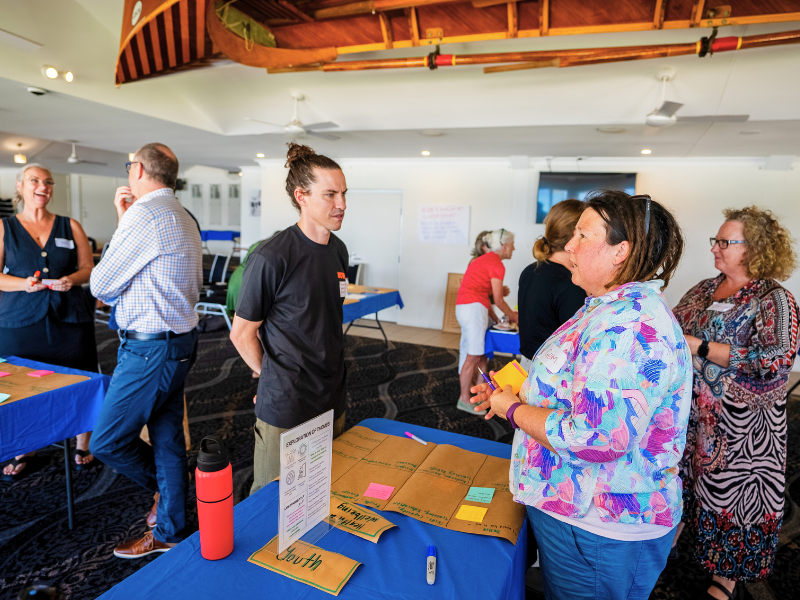Community workshop participants discussing ideas around tables indoors