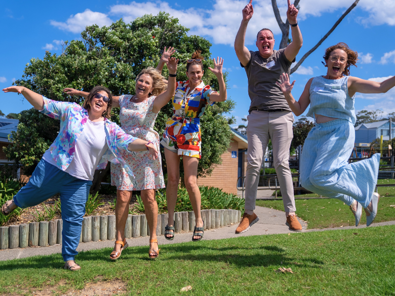Five adults jumping joyfully in sunny park