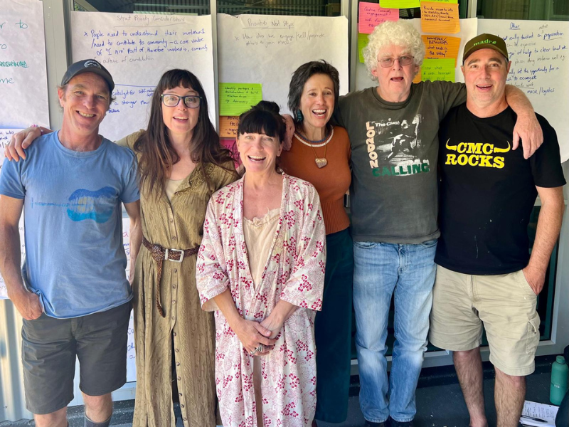 Group of people standing together with their arms around each other's shoulders.
